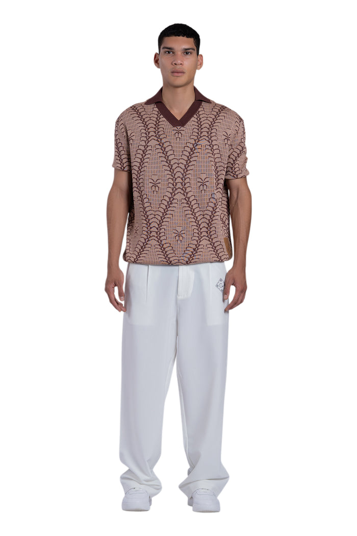 Man wearing a patterned brown shirt and white pants on a white background